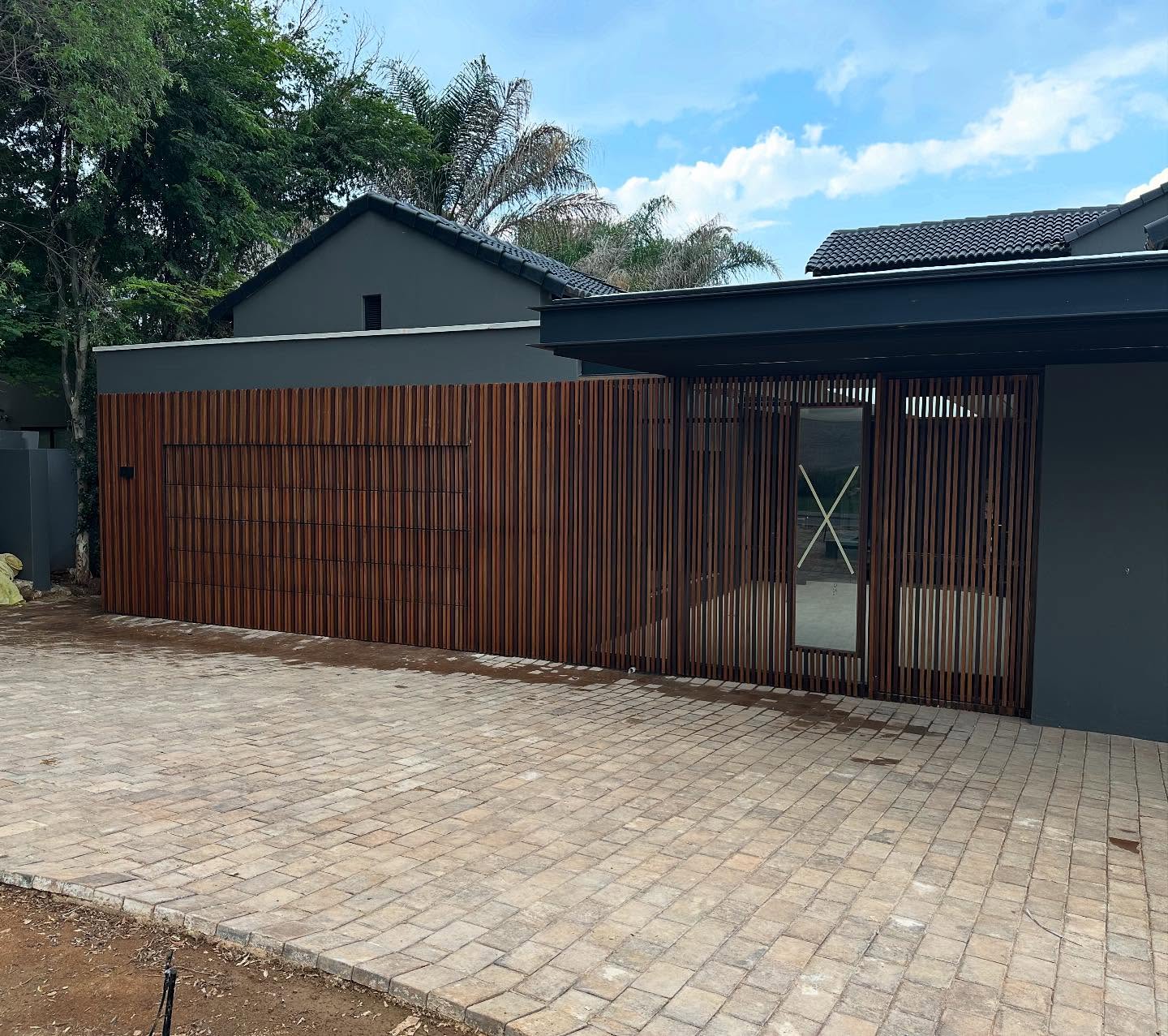 Vertical timber slat facade with a mesh accent panel beside a paved driveway
