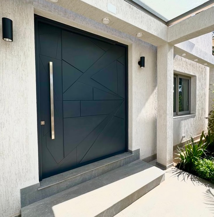 Dark angular geometric timber front door with a stainless steel pull handle