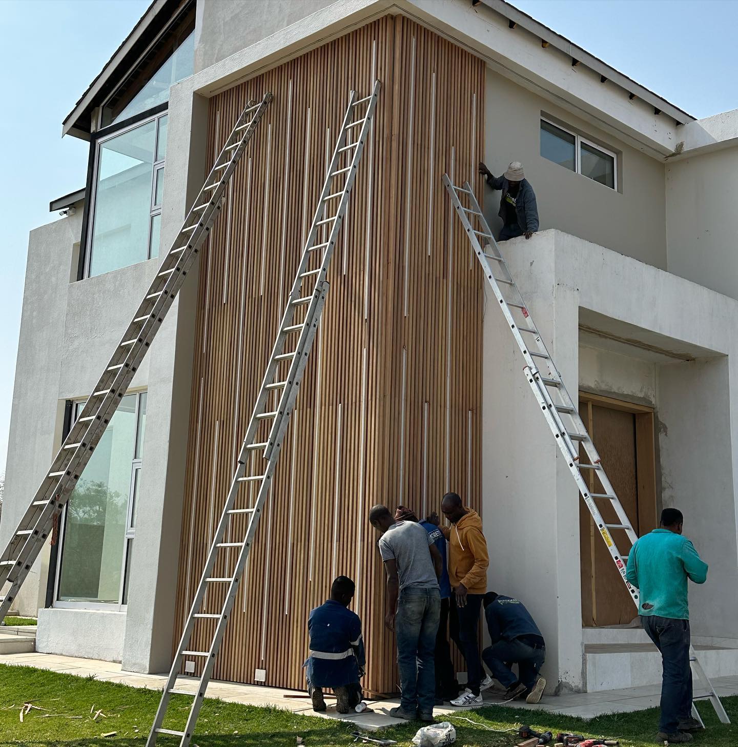 Installers on ladders fitting a vertical timber slat facade