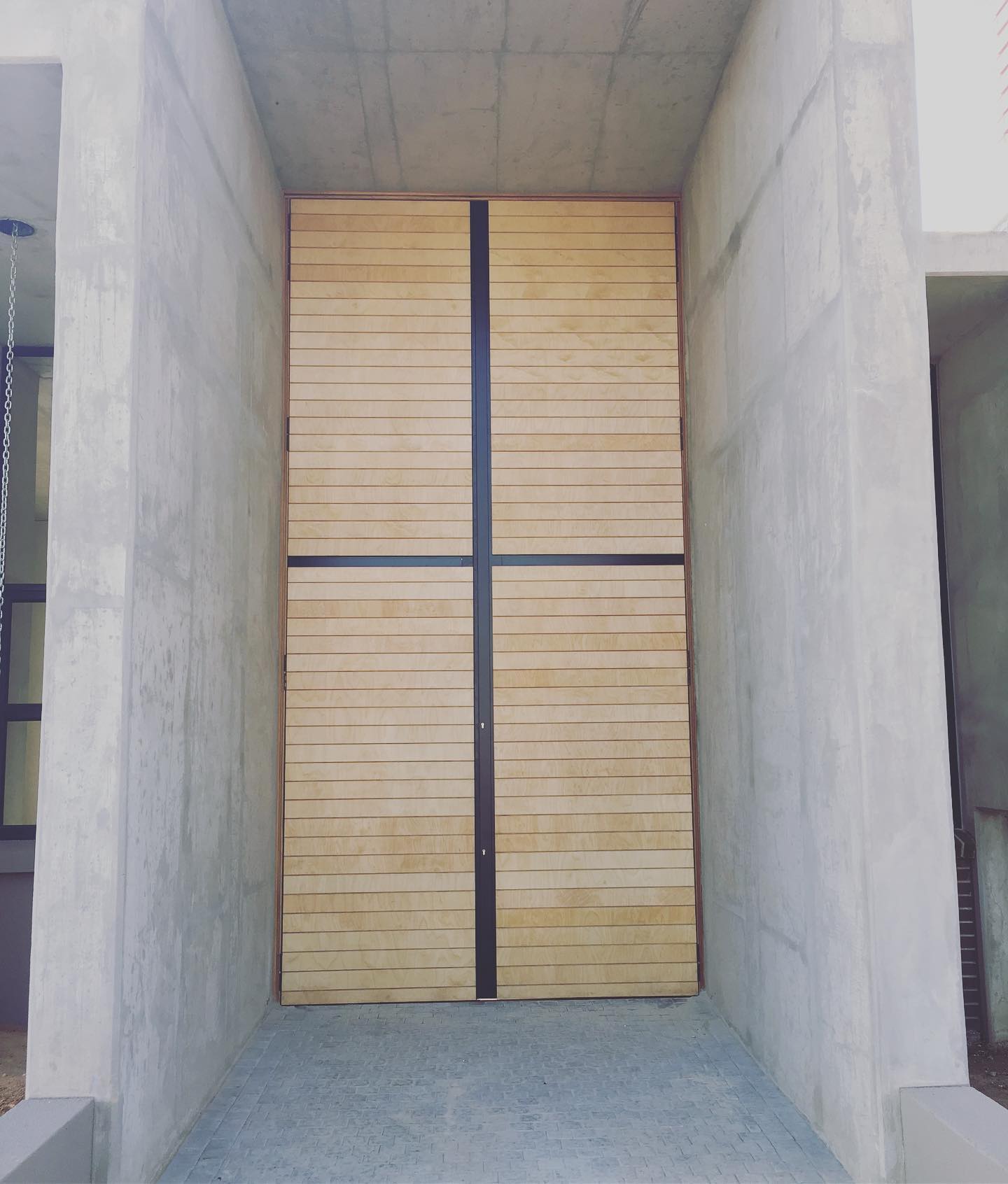 Horizontal slat double gate with black cross battens set in a concrete surround