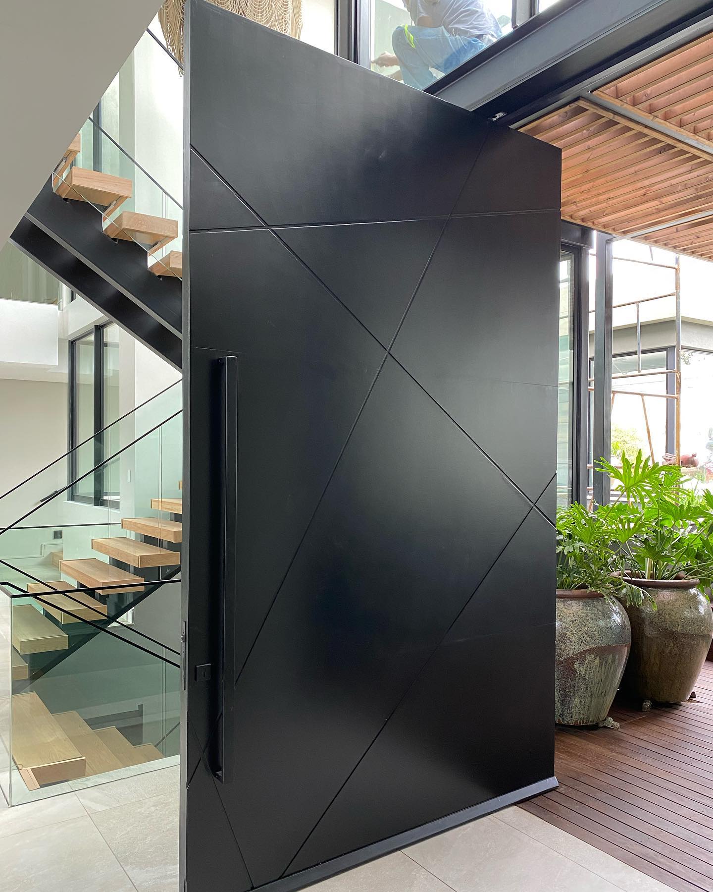 Angular black pivot door beside a glass and timber staircase