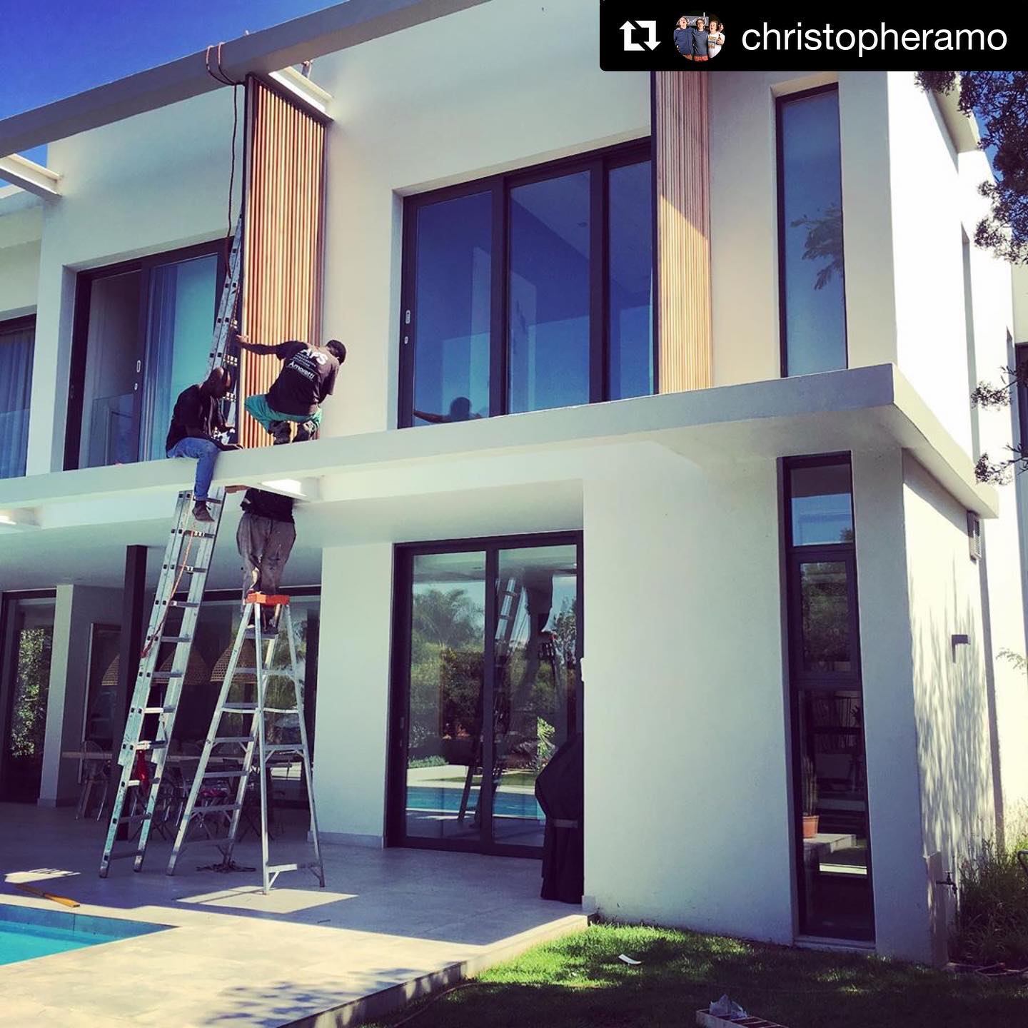 Installers on ladders fitting a vertical timber slat facade above a pool