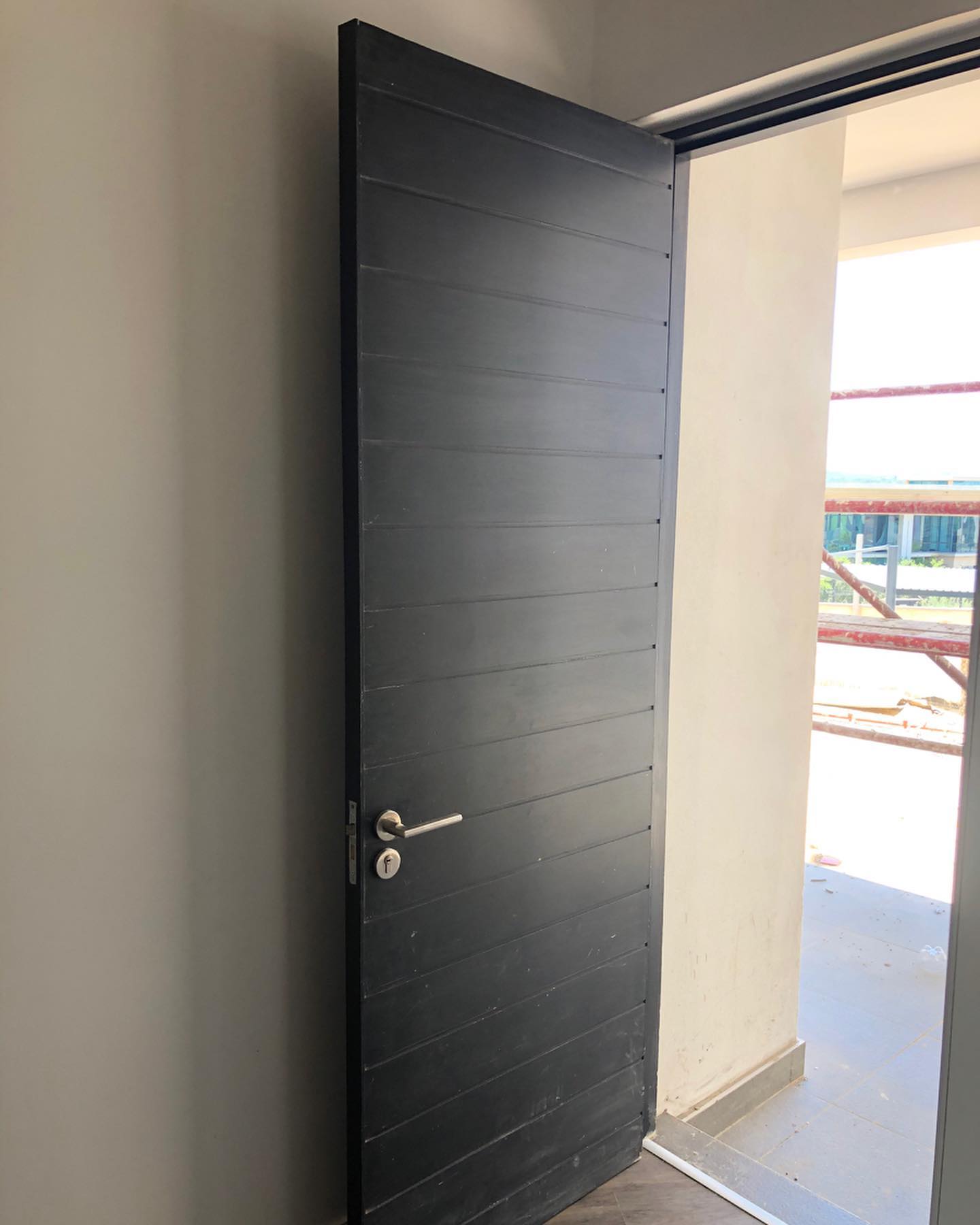 Black horizontal-slat door opening onto a construction site