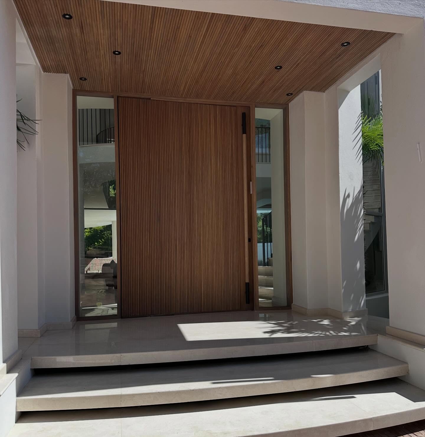 Timber slat pivot door entrance beneath a slatted timber ceiling canopy