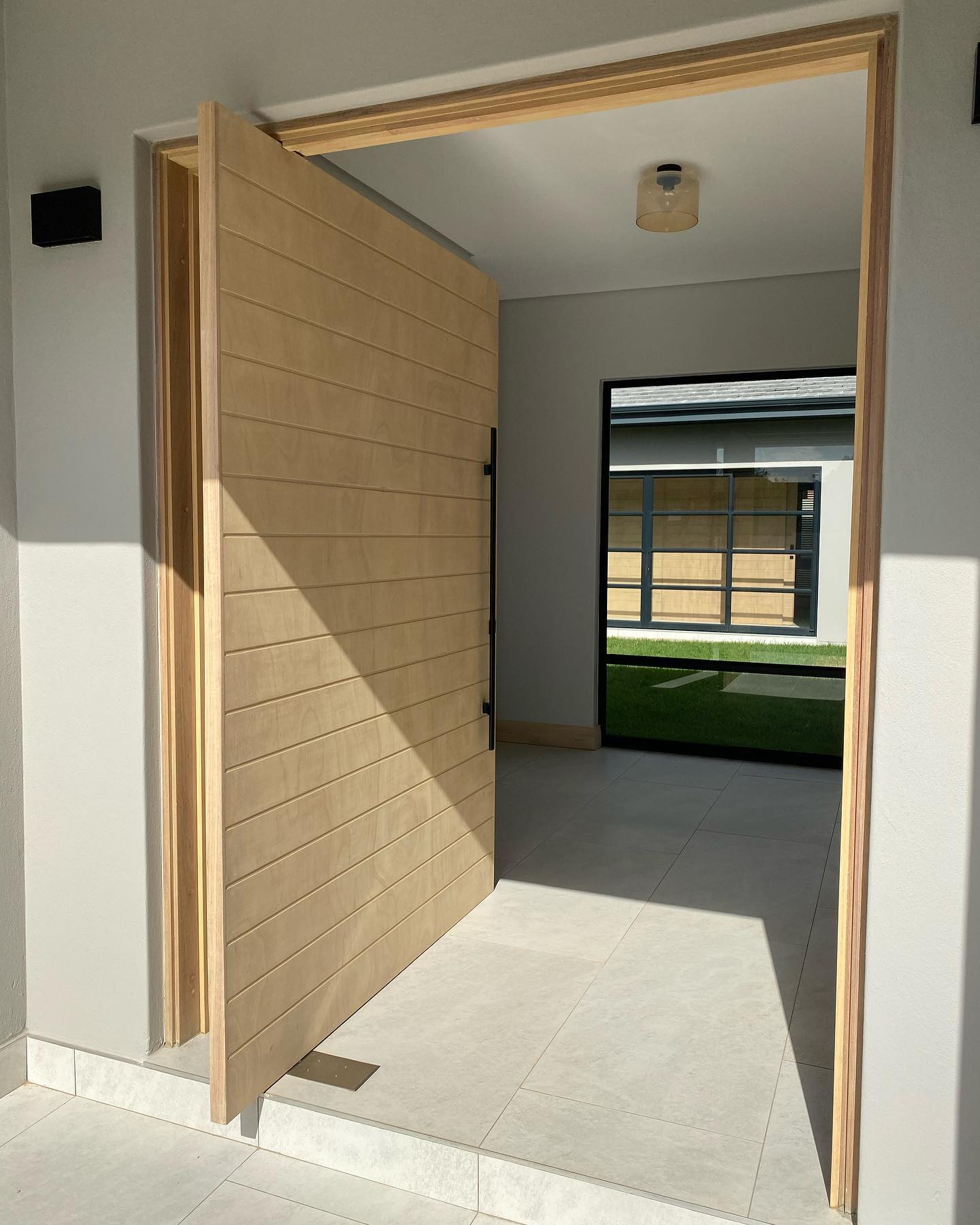 Light oak pivot door open, with a view through to a second courtyard