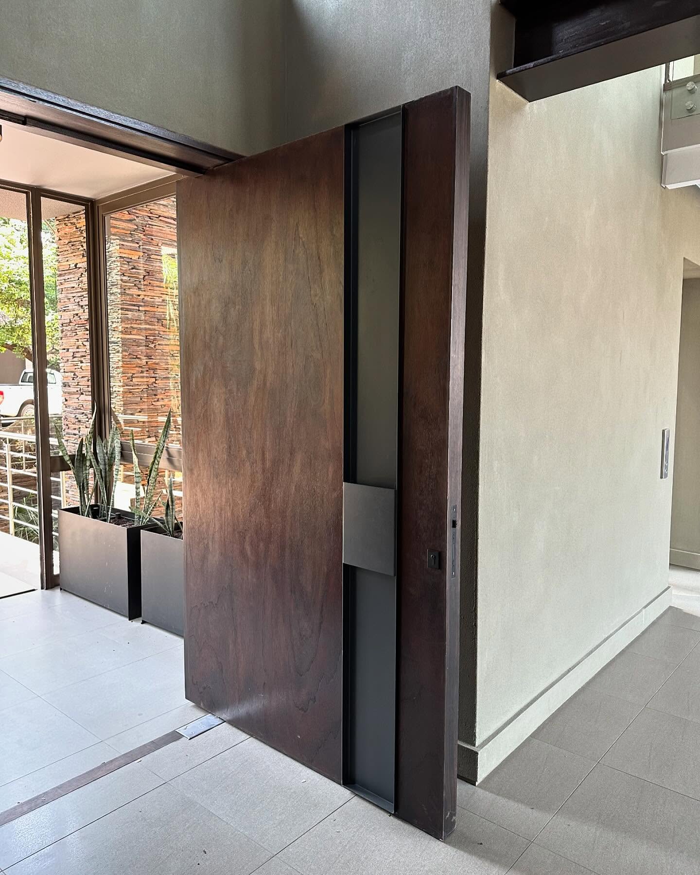 Oversized dark timber pivot door with an inset glass strip