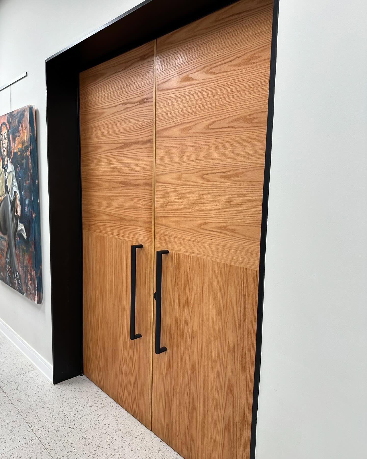 Oak double door with black bar handles in a gallery interior