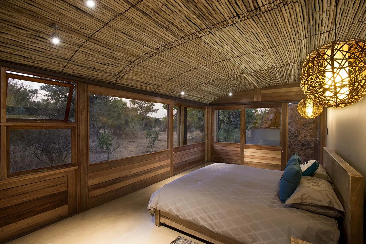 Bush Residence bedroom with full-height timber-framed windows overlooking bushveld