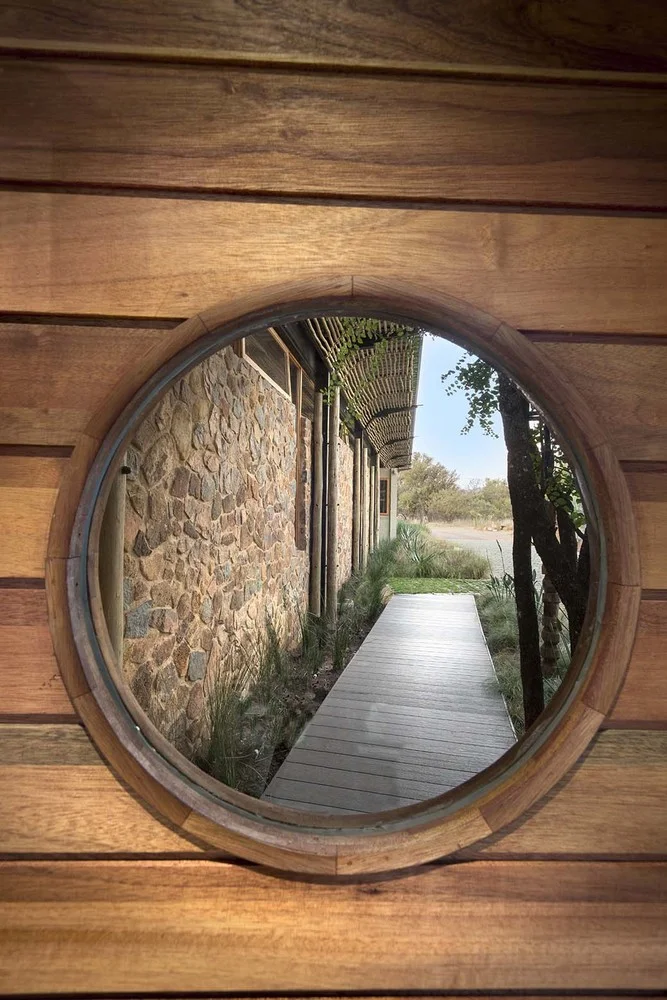 Bush Residence round timber-framed window looking down a stone-walled walkway